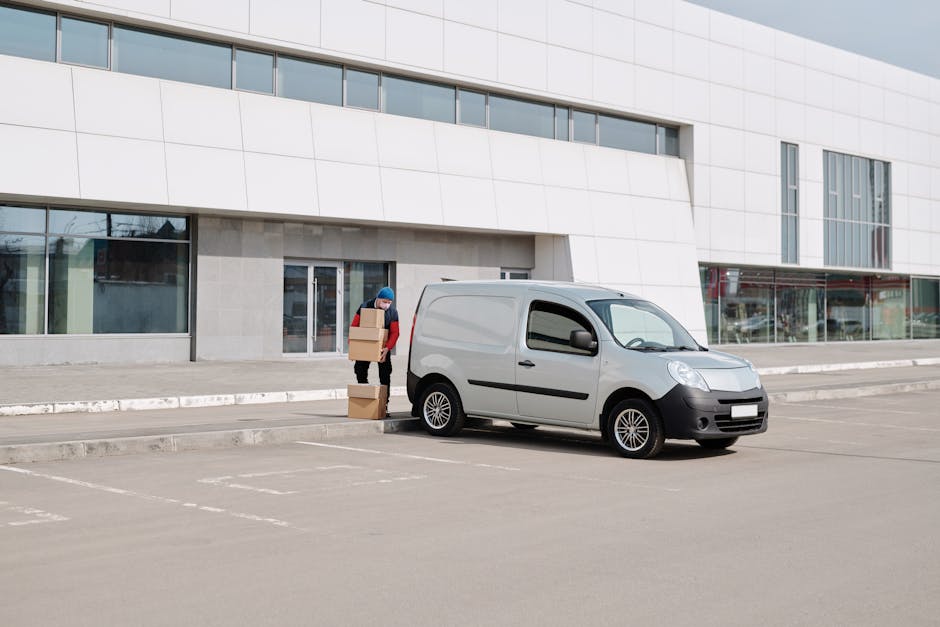 Two movers from Man with Van Dartmouth Park are engaged in a home relocation process outside a residential property, preparing to load cardboard boxes and packing materials into a white van. One mover