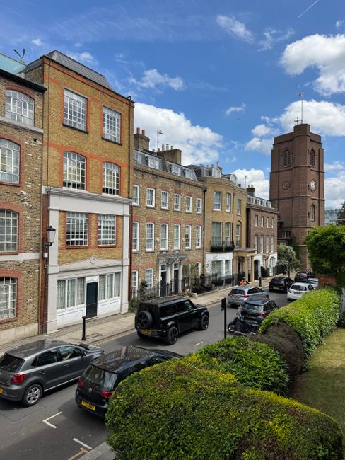 The image depicts the facade of a multi-storey, classical-style building with a white exterior, tall windows, and decorative architectural elements such as cornices and balustrades. The ground floor f